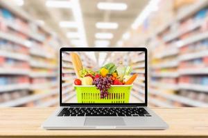 supermercato corridoio sfocato sfondo con il computer portatile computer e shopping cestino su legna tavolo drogheria in linea concetto foto