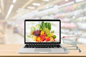 supermercato corridoio sfocato sfondo con il computer portatile computer e shopping carrello su legna tavolo drogheria in linea concetto foto