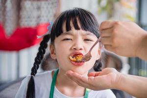 madre mano Tenere un' forchetta per alimentazione sua asiatico figlia pollo pepite. foto