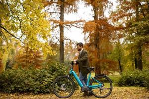 giovane con bicicletta elettrica nel parco autunnale foto