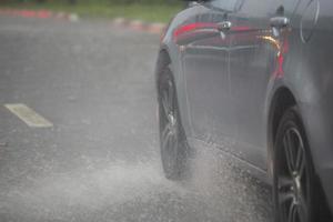 pioggia acqua spruzzo flusso a partire dal ruote di argento auto in movimento veloce nel luce del giorno città con selettivo messa a fuoco. foto