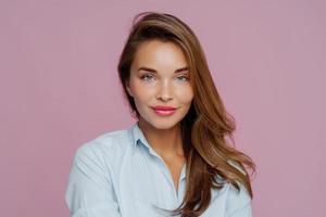 il primo piano della bella signora europea ha gli occhi azzurri, le labbra dipinte di rosso, la pelle sana, i capelli lunghi, guarda direttamente la telecamera, indossa la maglietta, posa su sfondo viola. bella donna pronta per il colloquio di lavoro foto