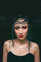 ritratto di giovane bellissimo donna piace strega con rosso labbra e nero corona su buio sfondo. nero buio bellezza, Halloween concetto foto