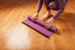 un' donna di mani posare su un' lilla yoga o fitness stuoia prima un' allenarsi pratica a casa su un' di legno pavimento. foto
