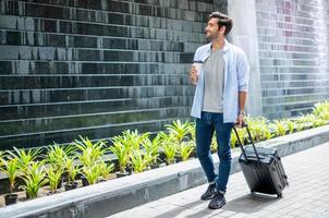 giovane caucasico uomo potabile caffè e traino il valigia in attesa il suo amico per viaggio insieme. foto