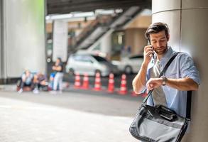 giovane caucasico uomo Guardando il tempo e chiamata su cellula Telefono mentre in attesa qualcosa nel davanti di il ufficio. foto