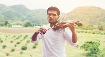 giovane musicista hipster che suona il violino nello stile di vita all'aperto della natura dietro la montagna. foto