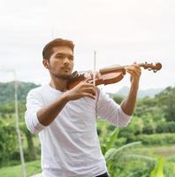 giovane musicista hipster che suona il violino nello stile di vita all'aperto della natura dietro la montagna. foto