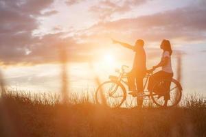 silhouette di dolce giovane coppia nel amore contento tempo su bicicletta foto