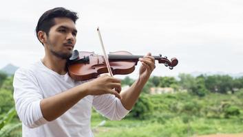 giovane musicista hipster che suona il violino nello stile di vita all'aperto della natura dietro la montagna. foto