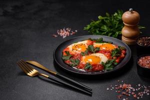 Shakshuka, un' piatto con fritte uova con pomodoro salsa, dolce Pepe, aglio, cipolle, spezie e erbe aromatiche foto