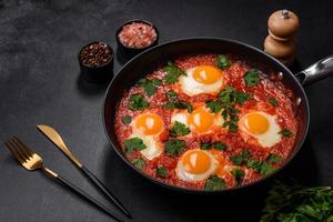 Shakshuka, un' piatto con fritte uova con pomodoro salsa, dolce Pepe, aglio, cipolle, spezie e erbe aromatiche foto