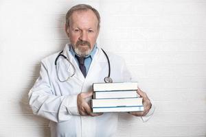 anziano medico detiene libri nel il suo mani consigliare autoeducazione e professionale sviluppo a qualunque età foto