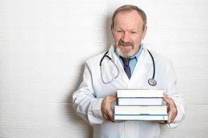 sorridente anziano medico detiene libri nel il suo mani consigliare autoeducazione e professionale sviluppo a qualunque età foto