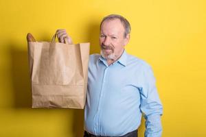 carino anziano uomo Tenere un' carta Borsa con acquisti nel il suo mani. foto