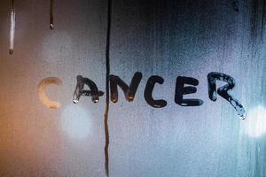 il parola cancro scritto di dito su notte bagnato bicchiere con sfocato strada leggero nel sfondo foto