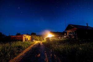 stellato notte cielo al di sopra di villaggio Casa nel estate. di legno Casa con uno lampadina leggero al di sopra di Entrata. Russia. foto