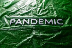 il parola pandemia di cui con argento lettere su spiegazzato verde plastica film sfondo. inclinato prospettiva. foto