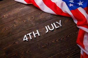il parole 4 ° luglio e spiegazzato Stati Uniti d'America bandiera su piatto strutturato di legno superficie sfondo foto