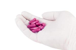 mano nel medico guanto Tenere plastica rosa colore biologico med capsule isolato su bianca sfondo avvicinamento foto