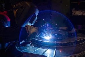 un' lente bagliore mentre Manuale semiautomatico elettrico saldatura con scintille, professionale industriale lavoratore nel nero protettivo maschera. foto