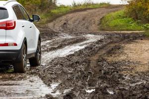 pulito bianca suv auto in movimento su sporco strada con bagnato argilla nel davanti di sfocato pendenza foto