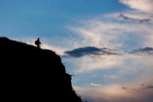 silhouette di fotografo con tripode su scogliera con sera blu cielo con nuvole sfondo foto