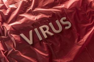 il parola virus di cui con argento metallo lettere su spiegazzato rosso plastica film con drammatico leggero foto