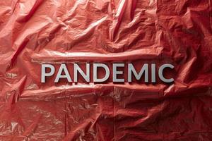 il parola pandemia di cui con argento lettere su rosso spiegazzato plastica film sfondo nel piatto posare composizione a centro foto