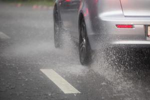 pioggia acqua spruzzo flusso a partire dal ruote di argento auto in movimento veloce nel luce del giorno città con selettivo messa a fuoco. foto