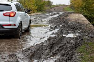 pulito bianca suv auto in movimento su sporco strada con bagnato argilla nel davanti di sfocato pendenza foto