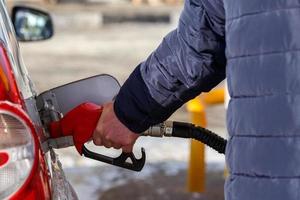 vecchio uomo mano nel blu caldo giacca rifornimento carburante grigio metallico auto su gas stazione a giorno tempo - avvicinamento con selettivo messa a fuoco foto