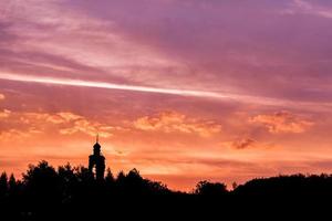 nero silhouette di Chiesa e foresta orizzonte su viola dorato tramonto cielo con morbido nuvole foto