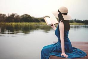 giovane donna rilassante di lungo il fiume. seduta su ponte e lettura libro. scollegato vita concetto foto