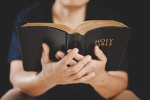 giovane donna persona mano Tenere santo Bibbia con studia a casa. adulto femmina cristiano lettura libro nel Chiesa. ragazza apprendimento religione spiritualità con pregare per Dio. concetto di alunno formazione scolastica fede. foto