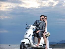 appena sposato coppia su il spiaggia cavalcata bianca scooter foto