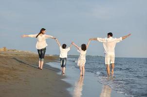 contento giovane famiglia avere divertimento su spiaggia a tramonto foto