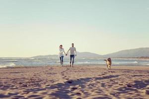 coppia con cane avendo divertimento su spiaggia su autunno giorno foto