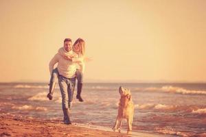 coppia con cane avendo divertimento su spiaggia su autunno giorno foto