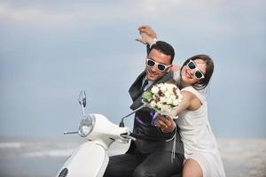 appena sposato coppia su il spiaggia cavalcata bianca scooter foto