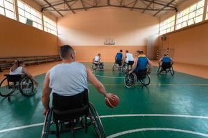 Disabilitato guerra veterani misto gara e età pallacanestro squadre nel sedie a rotelle giocando un' formazione incontro nel un' gli sport Palestra sala. portatori di handicap persone reinserimento e inclusione concetto foto