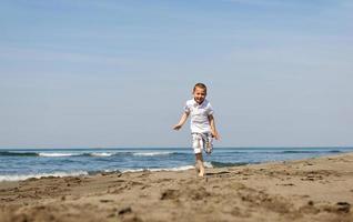 poco ragazzo in esecuzione su spiaggia foto