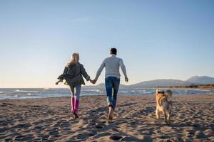 coppia con cane avendo divertimento su spiaggia su autunno giorno foto