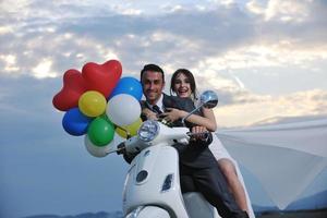 appena sposato coppia su il spiaggia cavalcata bianca scooter foto