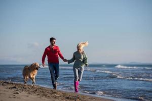 coppia con cane avendo divertimento su spiaggia su autunno giorno foto