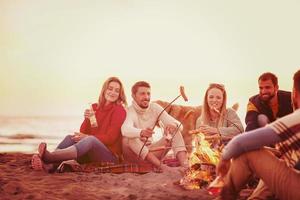 gruppo di giovane amici seduta di il fuoco a spiaggia foto