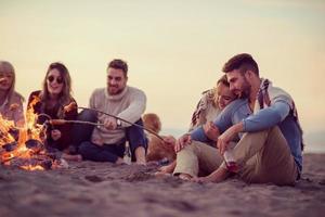 gruppo di giovane amici seduta di il fuoco a spiaggia foto