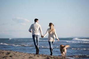 coppia con cane avendo divertimento su spiaggia su autunno giorno foto