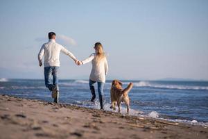 coppia con cane avendo divertimento su spiaggia su autunno giorno foto