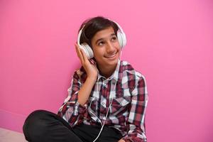 Arabo adolescenziale ragazzo indossare cuffie e ascoltando per musica rosa sfondo foto